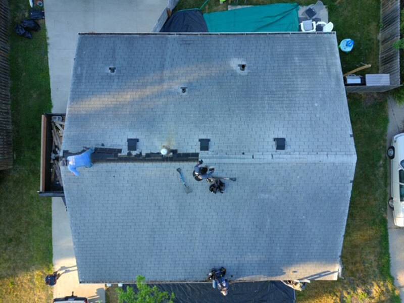 Aerial view of a house with an old gray roof with three workers starting on replacement
