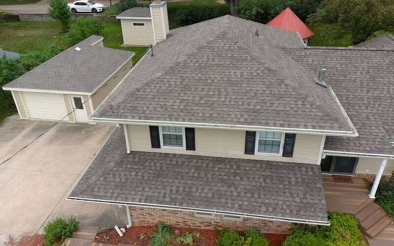 Angled aerial view of a tan one-and-a-half story house with a detached single car garage on the left side
